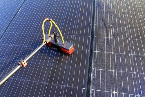 A close-up of a brush with yellow and black attachments cleaning a solar panel, with another clean solar panel visible beside it.